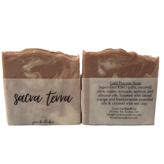 Two bars of Sacra Terra soap with labels and product details on a neutral background